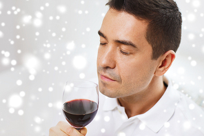 profession, drinks, leisure and people concept - happy man drinking and smelling red wine from glass over snow effect