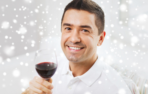 profession, drinks, leisure, holidays and people concept - happy man drinking red wine from glass over snow effect