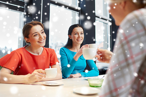people, leisure, friendship and communication concept - happy young women meeting and drinking tea or coffee at cafe over snow effect