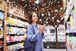 sale, shopping, consumerism and people concept - happy young woman taking notes to notebook in grocery store or market over snow effect