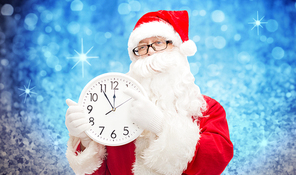 christmas, holidays, time and people concept - man in costume of santa claus with clock showing twelve pointing finger over blue glitter or lights background