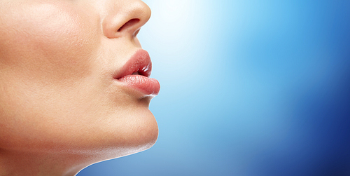 beauty, people, make-up and plastic surgery concept - close up of young woman lips over blue background
