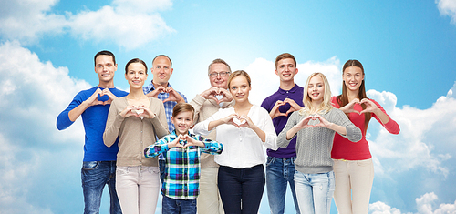 gesture, family, generation and people concept - group of smiling men, women and boy showing heart shape hand sign over blue sky and clouds background