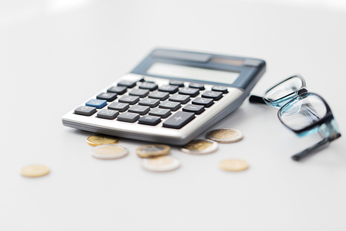 business, finance, money and bookkeeping concept - calculator, eyeglasses and euro coins on office table