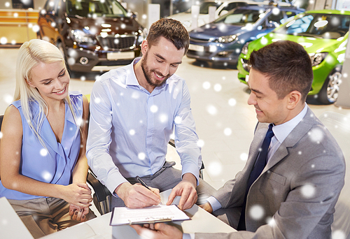 auto business, sale and people concept - happy couple with dealer buying car and signing documents in auto show or salon over snow effect