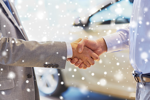 auto business, car sale, deal, gesture and people concept - close up of male handshake in auto show or salon over snow effect