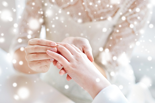 people, homosexuality, same-sex marriage and love concept - close up of happy lesbian couple hands putting on wedding ring over snow effect