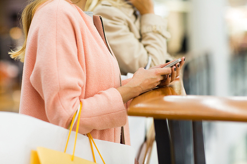 sale, consumerism, technology and people concept - close up of young women with smartphones and shopping bags in mall