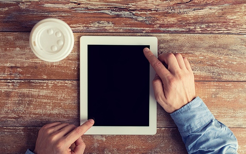 business, education, people and technology concept - close up of male hands with tablet pc computer and coffee paper cup on table