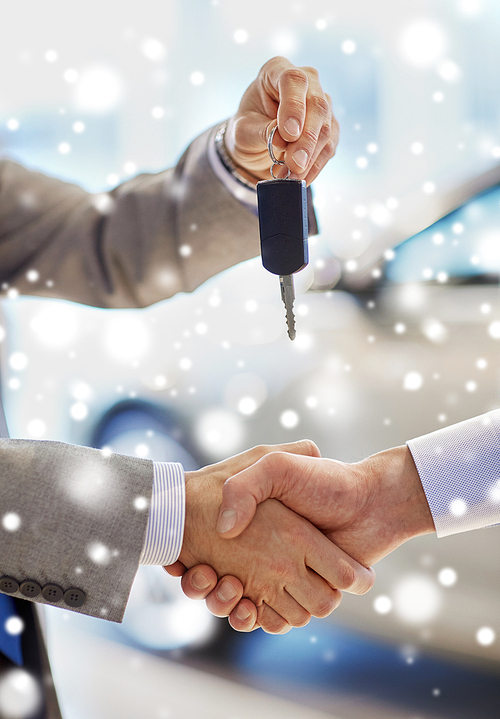 auto business, car sale, deal, gesture and people concept - close up of dealer giving key to new owner and shaking hands in auto show or salon over snow effect