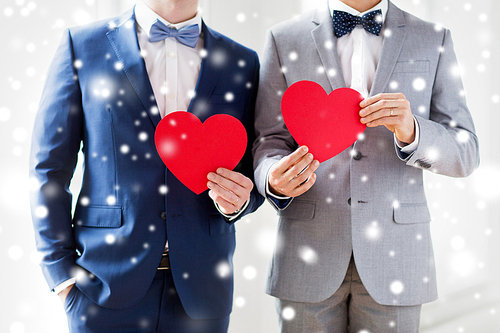 people, homosexuality, same-sex marriage, valentines day and love concept - close up of happy married male gay couple holding red paper heart shapes on wedding over snow effect