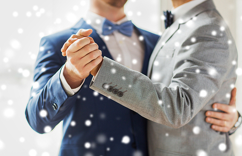 people, homosexuality, same-sex marriage and love concept - close up of happy male gay couple holding hands and dancing on wedding over snow effect