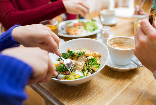 people, leisure and food concept - close up friends having dinner and eating at restaurant