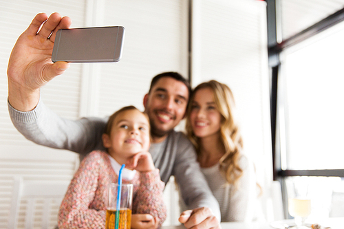 family, parenthood, technology and people concept - close up of happy mother, father and little girl having dinner and taking selfie by smartphone at restaurant