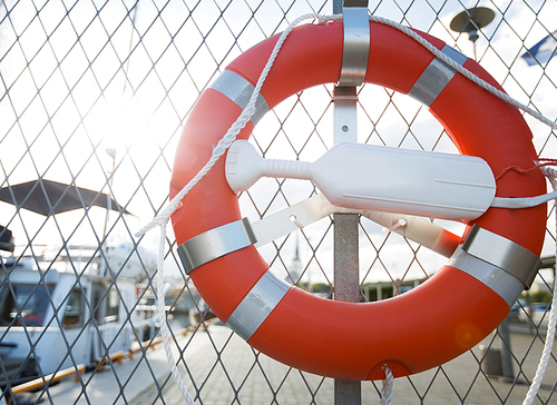 sailing, safety and life rescuing concept - lifebuoy hanging on fence over moored boats on pier