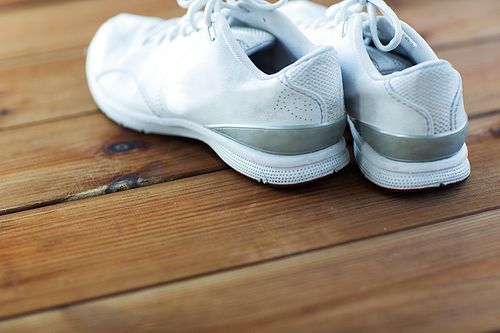 sport, fitness, shoes, footwear and objects concept - close up of sneakers on wooden floor