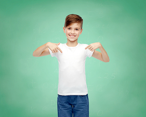 school, education, childhood, advertisement and people concept - happy boy in white t-shirt and jeans pointing finger to himself over green chalk board background