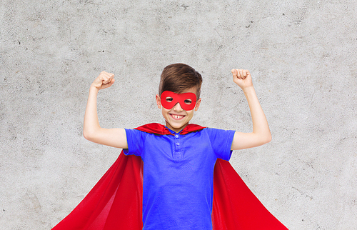 carnival, childhood, power, gesture and people concept - happy boy in red super hero cape and mask showing fists over gray background