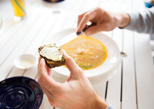 restaurant, couple and holiday concept - close up of hands applying and spreading butter to bread