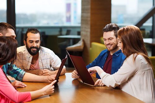 leisure, people and holidays concept - smiling friends discussing menu at restaurant