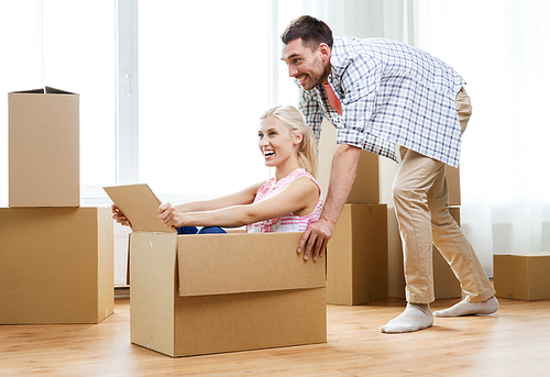 home, people, moving and real estate concept - happy couple having fun and riding in cardboard boxes at new home