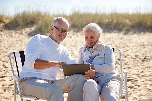 family, age, travel, tourism and people concept - happy senior couple with tablet pc computer resting in folding chairs on summer beach