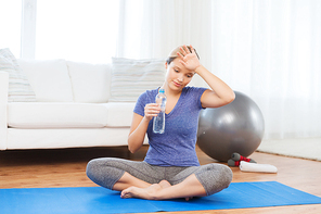 fitness, sport, people and healthy lifestyle concept - tired woman with bottle of water after exercising on mat at home