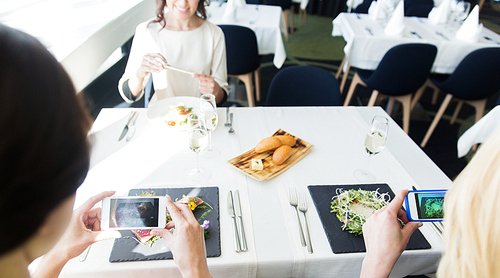 people, holidays, technology and lifestyle concept - close up of women with smartphones taking picture of food at restaurant