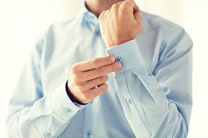people, business, fashion and clothing concept - close up of man fastening buttons on shirt sleeve at home