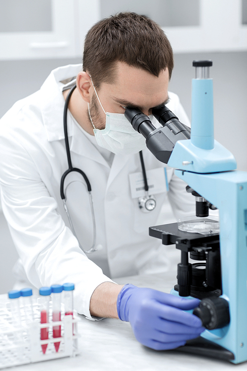 science, medicine, technology, biology and people concept - young male scientist with test tubes looking to microscope and making or research in clinical laboratory