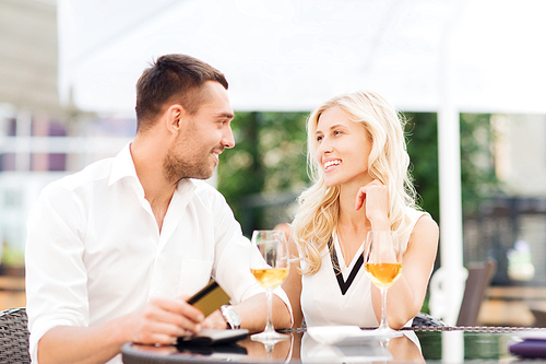 date, people, payment and relations concept - happy couple with credit card, bill and wine glasses at restaurant terrace