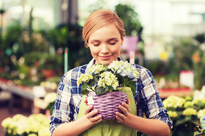 people, gardening and profession concept - happy woman or gardener smelling flowers in greenhouse