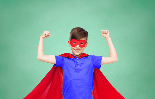 school, education, childhood, power and people concept - happy boy in red super hero cape and mask showing fists over green chalk board background