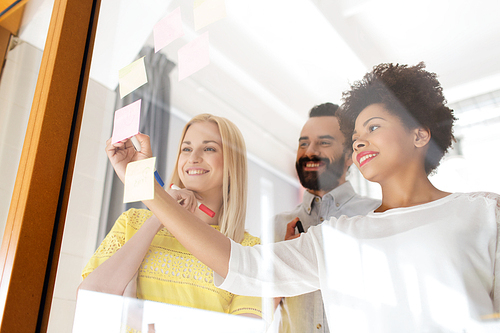 business, startup, planning, management and people concept - happy international creative team writing on stickers at office glass board