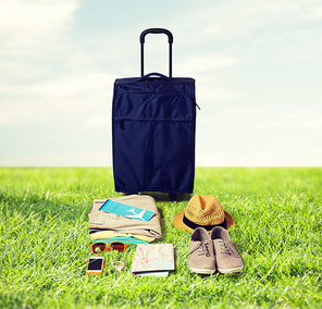 summer vacation, tourism and objects concept - travel bag, map, air ticket and clothes with personal stuff over blue sky and grass background