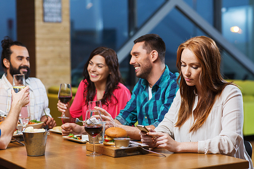 leisure, technology, internet addiction, lifestyle and people concept - woman with smartphone and friends at restaurant