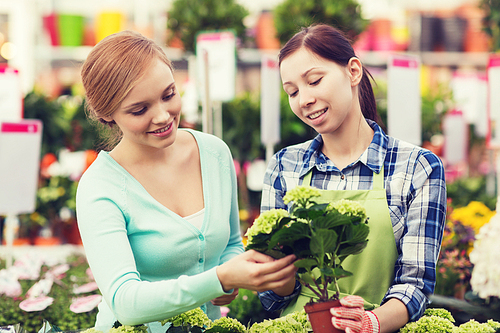 people, gardening, shopping, sale and consumerism concept - happy gardener helping woman with choosing flowers in greenhouse