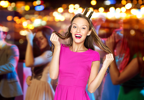 people, holidays, celebration and glamour concept - happy young woman or teen girl in pink dress and princess crown at night club party over crowd and lights background