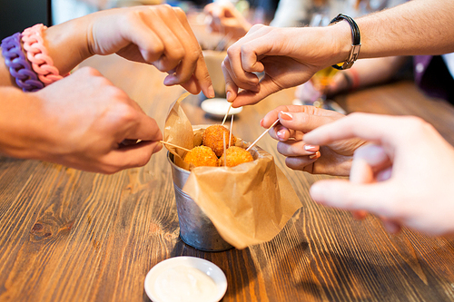 fast food, junk food, unhealthy eating and culinary concept - close up of people hands taking cheese balls with skewers at bar or restaurant