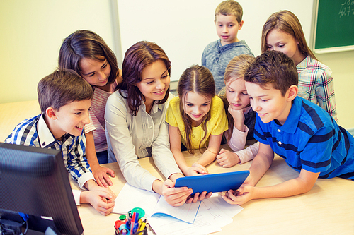 education, elementary school, learning, technology and people concept - group of school kids with teacher looking to tablet pc computer in classroom