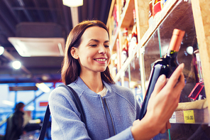 sale, shopping, consumerism and people concept - happy young woman choosing and buying wine in market