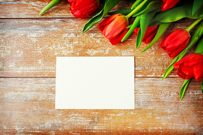advertisement, valentines day, greeting and holidays concept - close up of red tulips and blank paper or letter on wooden background