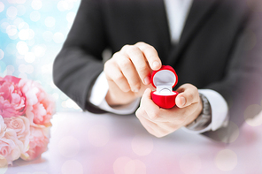 people, holidays, presents and proposal concept - close up of man with gift box and engagement ring over holidays lights background