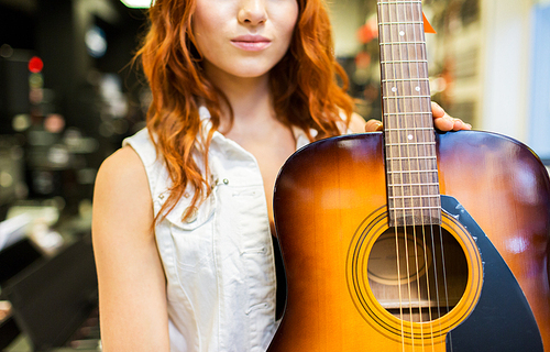 music, sale, people, musical instruments and entertainment concept - close up of female assistant or customer holding acoustic guitar at music store