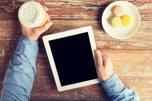 business, education, people and technology concept - close up of male hands with tablet pc computer, cookies and coffee cup on table