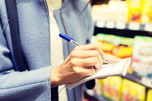 sale, shopping, consumerism and people concept - close up of young woman with pen taking notes to notebook in market