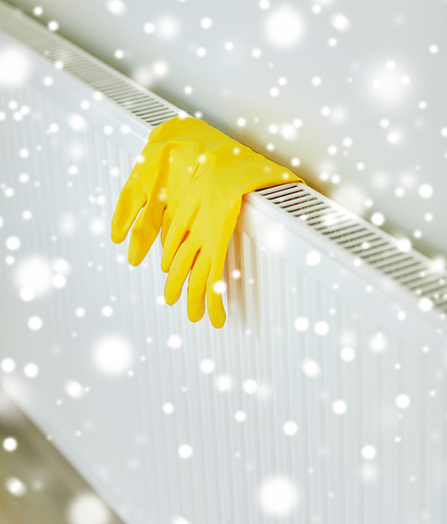 protection, housework and housekeeping concept - close up of yellow rubber gloves hanging on heater at home over snow effect