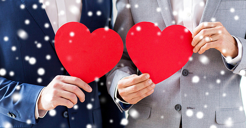 people, homosexuality, same-sex marriage, valentines day and love concept - close up of happy married male gay couple holding red paper heart shapes on wedding over snow effect