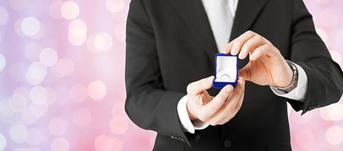 people, holidays, presents and proposal concept - close up of man with gift box and engagement ring over holidays lights background