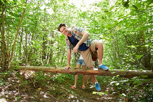 adventure, travel, tourism, hike and people concept - group of smiling friends walking with backpacks and climbing over fallen tree trunk in woods